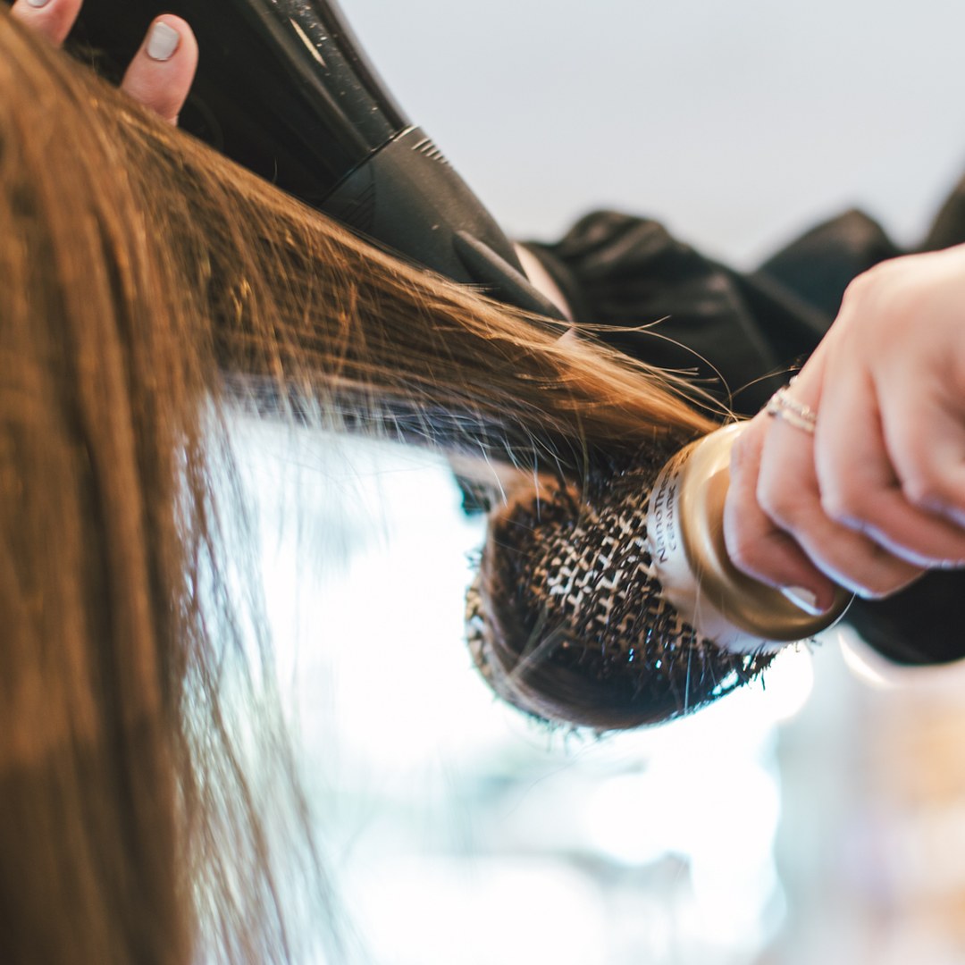 A stylist shapes hair with a round brush and dryer at Absolute Hair